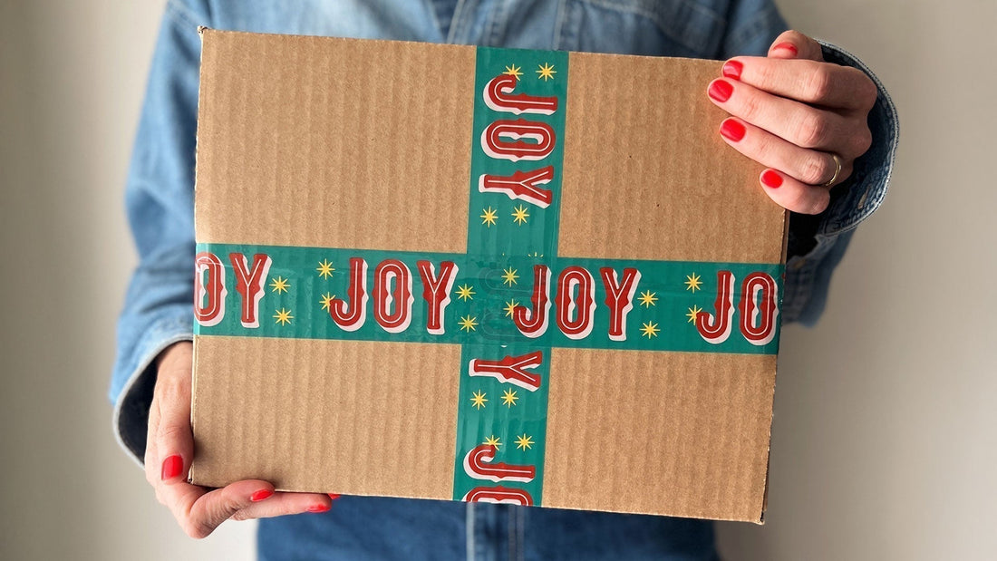 A woman holiday a gift box sealed with cute red and green packing tape with Joy printed on it.