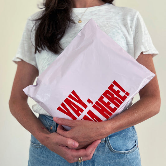 Person holding a pink poly mailer for Poshmark resellers with red printed text that says Yay I'm Here!