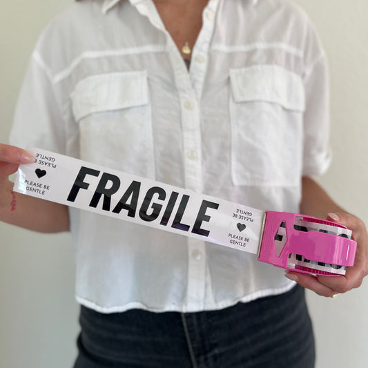 Woman holding a mini roll of cream packing tape with black Fragile text in a pink dispenser.
