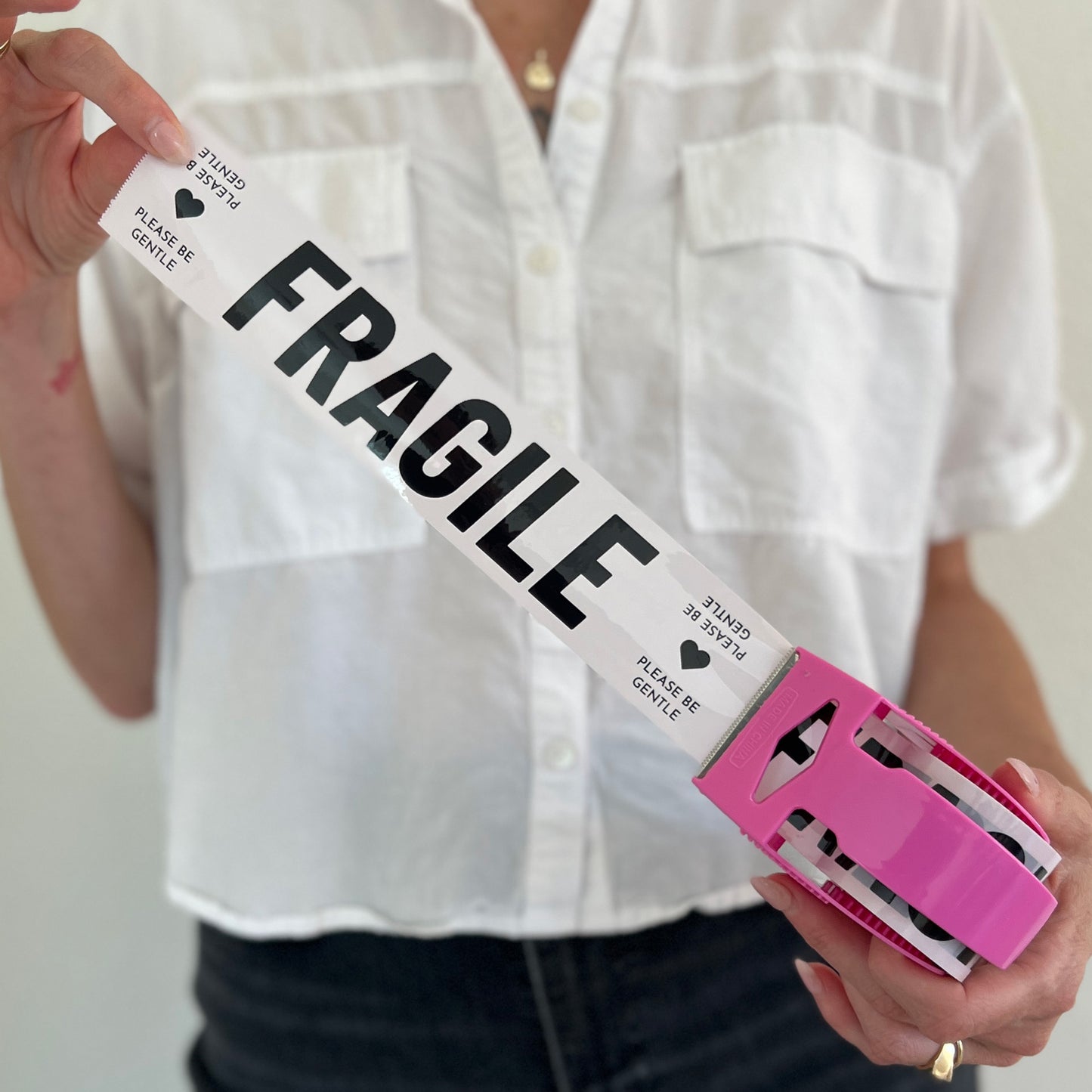 Woman holding a mini roll of cream packing tape with black Fragile text in a pink dispenser.