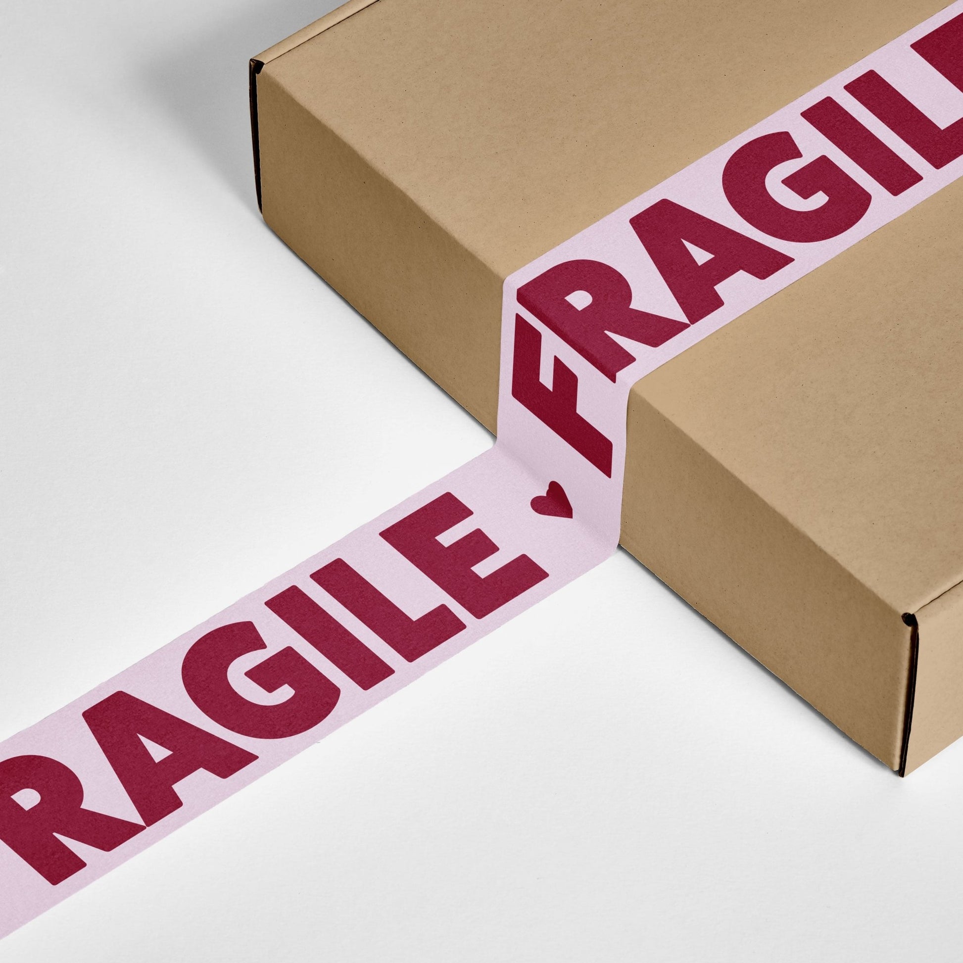 A cardboard box sealed with pink packing tape that reads “Fragile” in bold burgundy text.