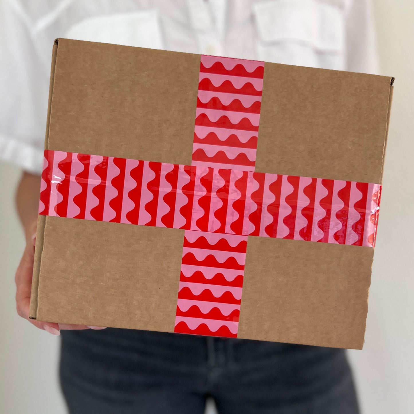 Woman holding a box sealed with pink and red wave packing tape—colorful, eye-catching tape perfect for small business packaging and gift shipping.