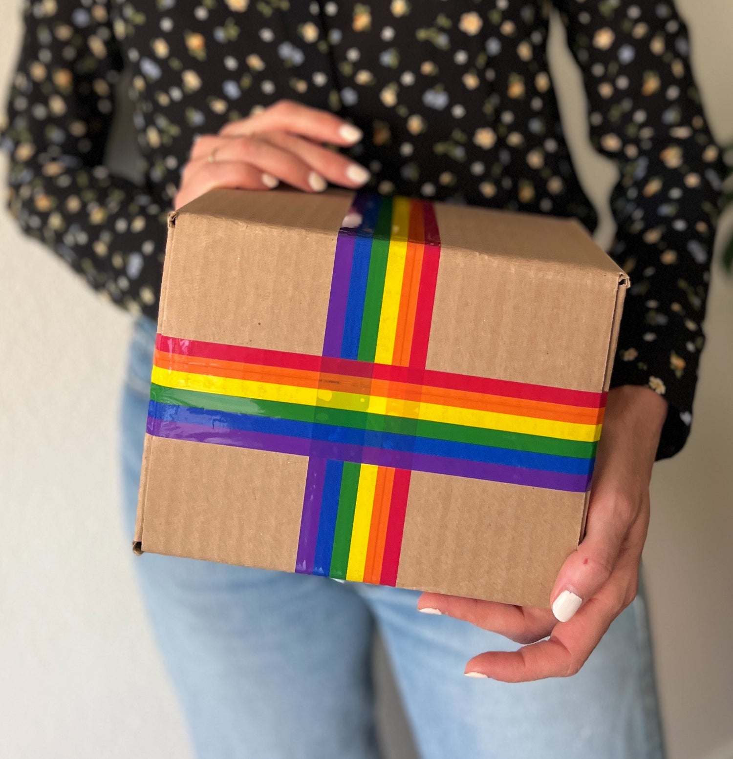 A woman holding a shipping box with cute rainbow pride packing tape on it.
