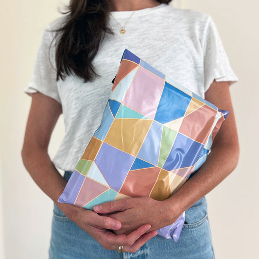 Person holding a cute and colorful geometric-patterned poly mailer shipping bag against a neutral background
