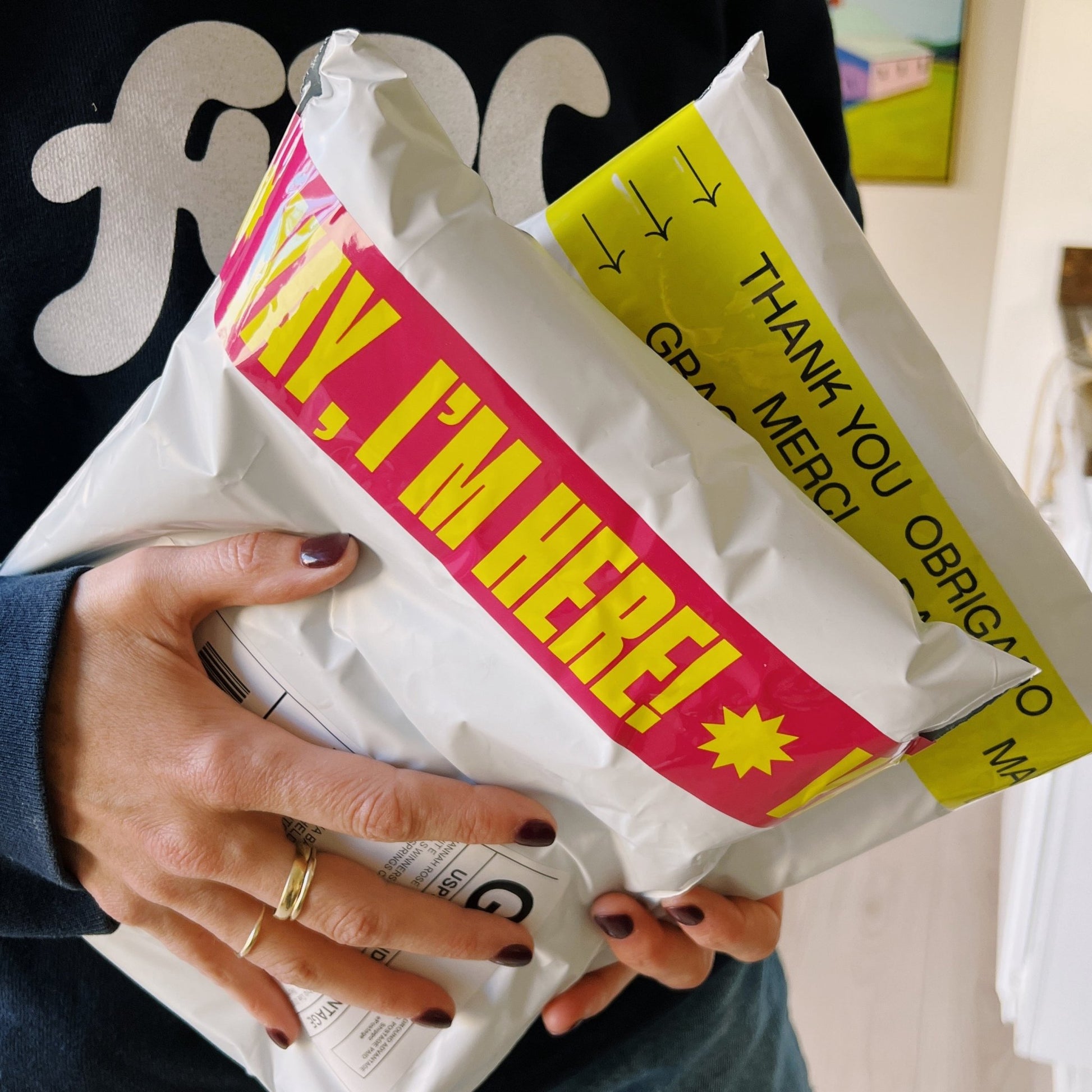 Woman holding white poly mailers sealed with bold pink packing tape that reads “Yay, I’m Here!” in bright yellow—fun, eye-catching shipping tape that adds personality and excitement to package deliveries.