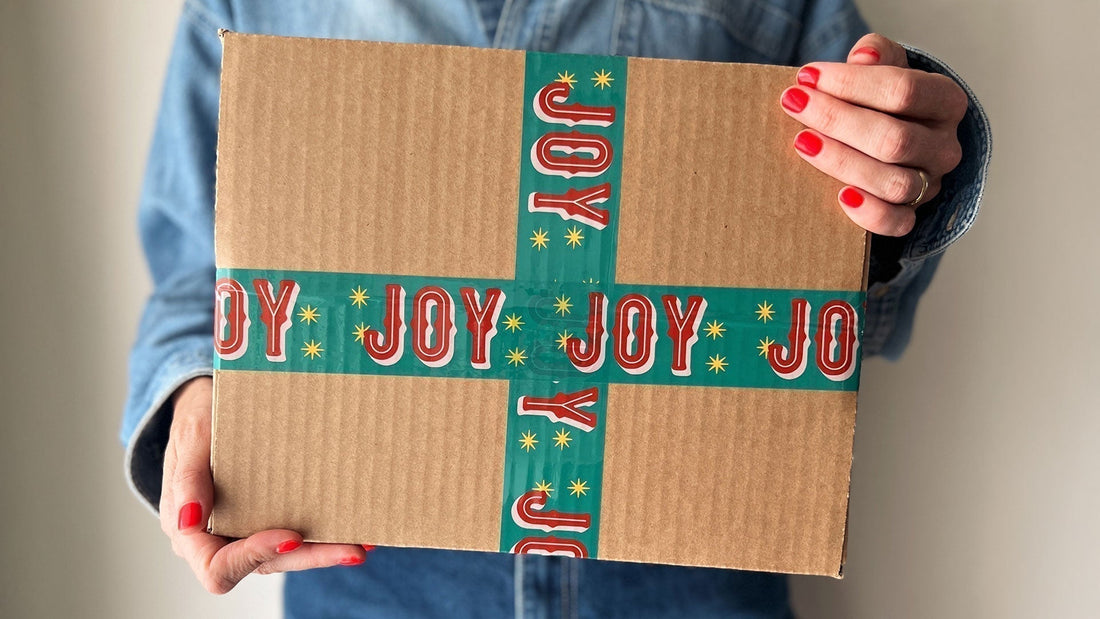 A woman holiday a gift box sealed with cute red and green packing tape with Joy printed on it.