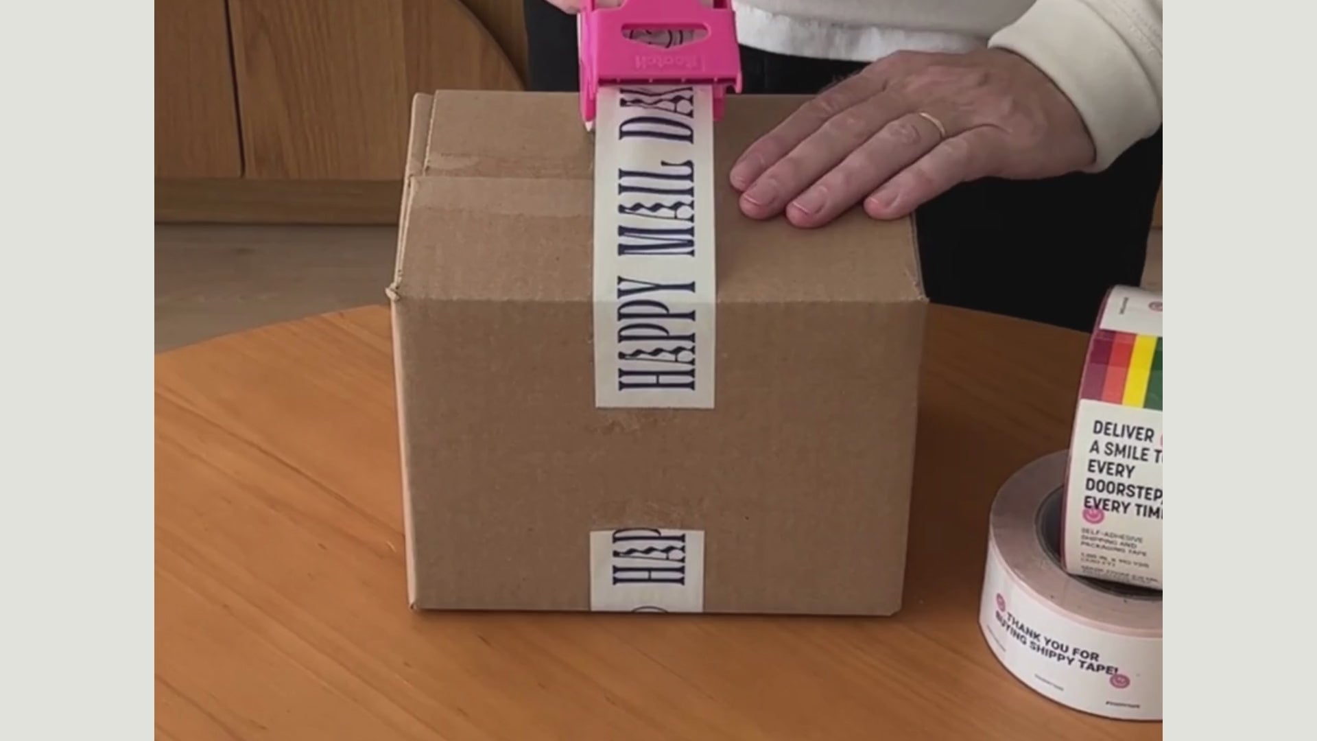 A man is adding a personal touch to a package by taping it with "Happy Mail Day" adhesive tape.